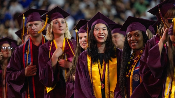 Students wearing maroon caps and gowns at an ASU graduation ceremony.