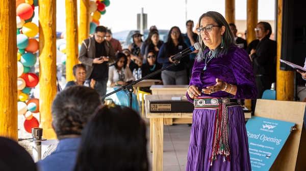 A woman in Native American dress addresses a crowd via microphone.