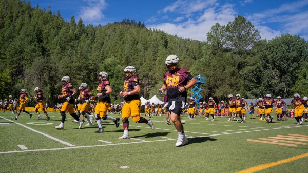 ASU football players on a field surrounded by pine trees