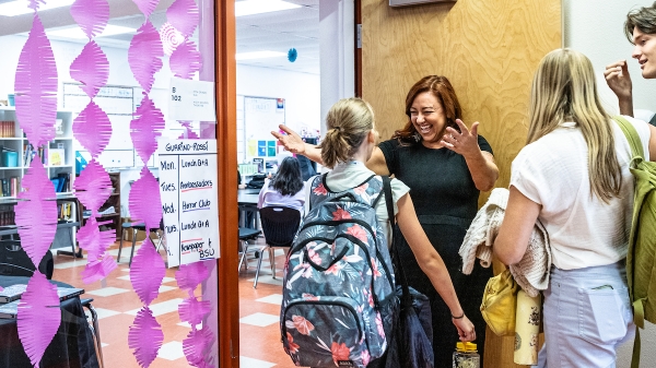 Teacher welcoming students into a classroom.