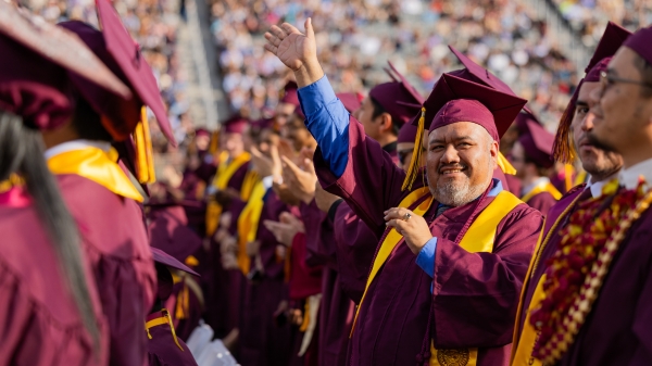 Man in cap and gown waving to family during ASU commencement