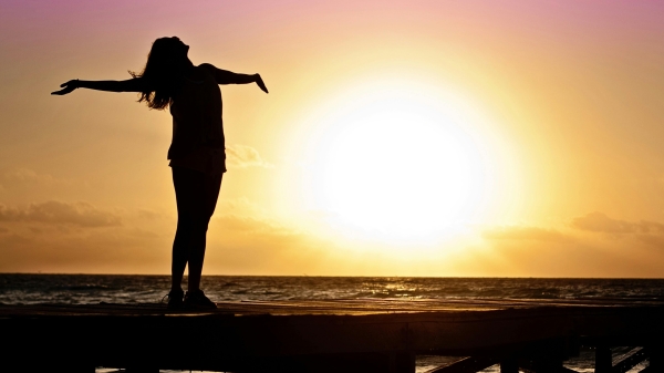A woman stretches out her arms towards the sun in celebration of a new year and new opportunities for personal growth