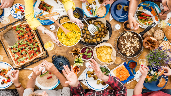 Bird's eye view of a food-filled table with hands passing food around.