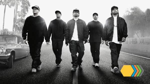 Black-and-white still image from the film "Straight Outta Compton" showing five men walking down the middle of a street.