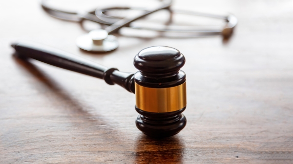 A gavel and stethoscope lay next to each other on a wooden surface. 