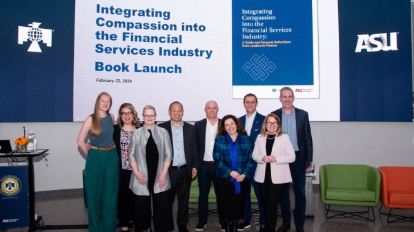 A group of people pose for a photo underneath a sign reading "Integrating Compassion into the Financial Services Industry Book Launch"