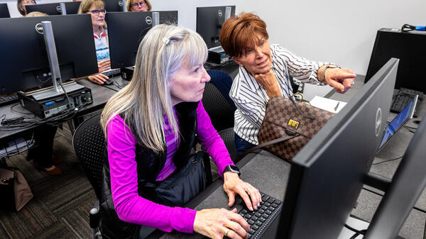 Two women seated next to each other work on computers.