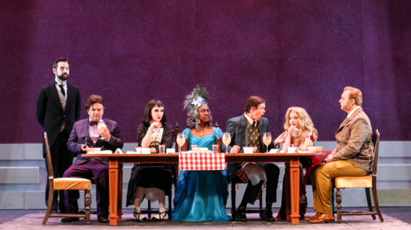 Six characters sit at a dining table with a butler to the left 