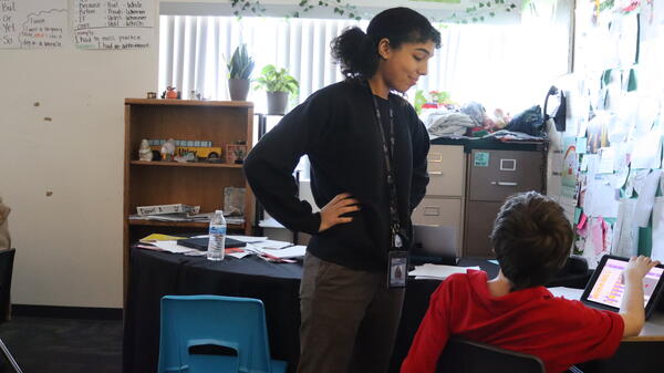 Teacher standing next to a student in a classroom.