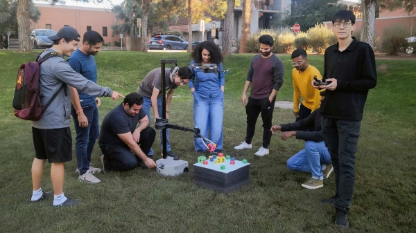 Assistant Professor Zhe Xu with students and their robots outside in a grassy area.
