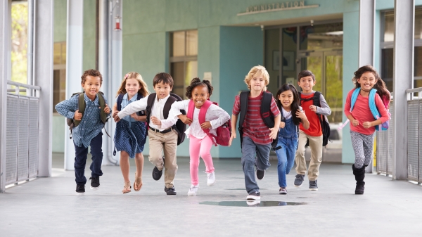 Eight elementary-age children run down the hall with their backpacks