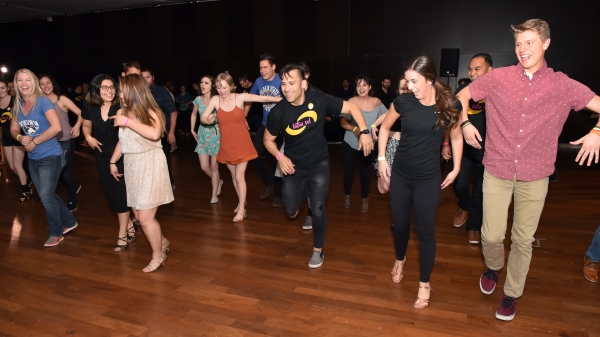 People stand on a wood floor, dancing and smiling