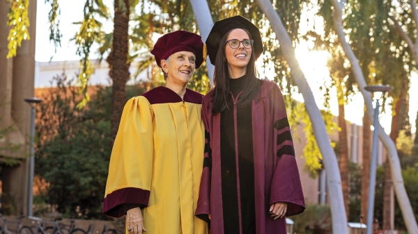 Two people posing in gold and maroon graduation robes