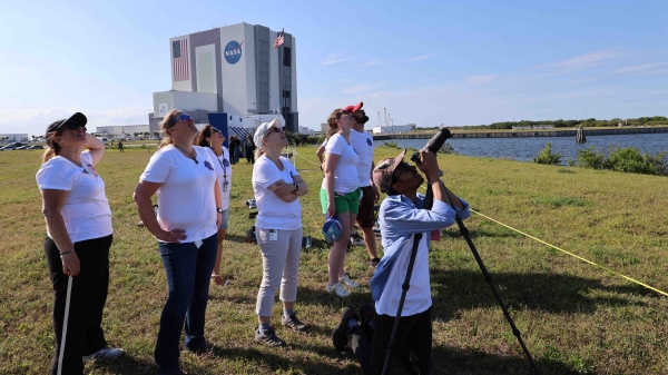 Group of people outdoors looking up the sky with a NASA building in the background.
