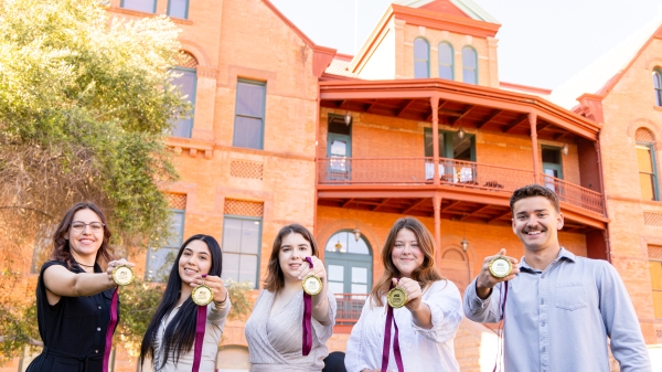 Five students holding Dean's Medalist medallions in front of Old Main.