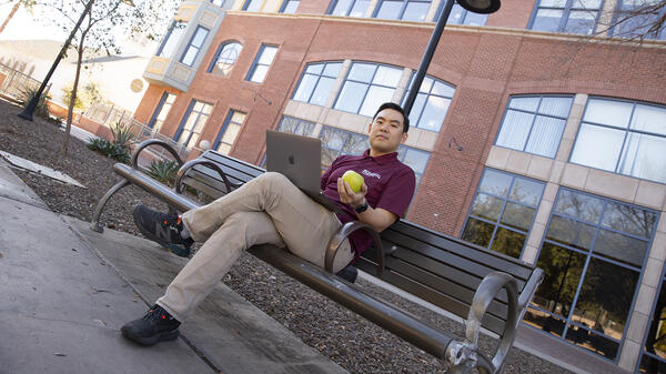 A portrait of Kookjin Lee sitting on a bench with a laptop