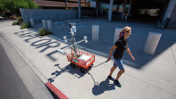 Woman pulling heat-measuring robot cart along a sidewalk