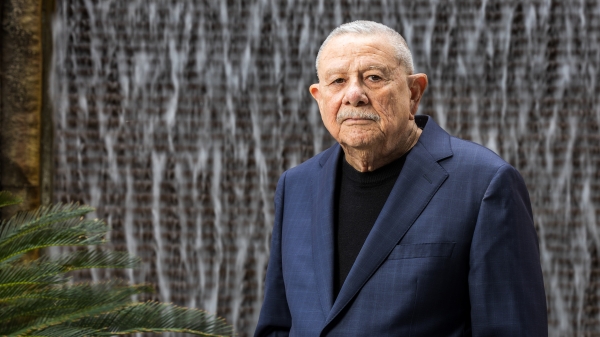 A man with gray hair stands in front of a water fountain