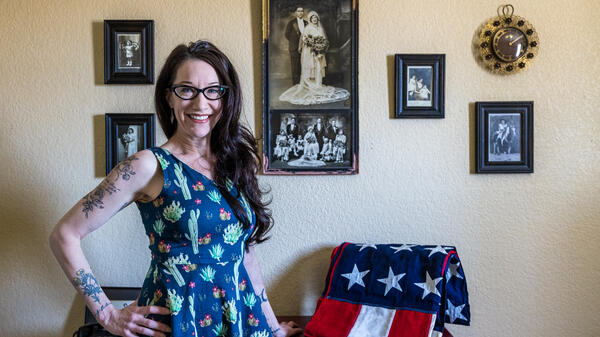 Woman with glasses and long dark hair poses for a photo in front of historical family photos and a folded American flag