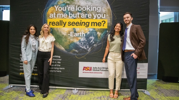 Four people stand around a sign that shows an image of earth and reads "You're looking at me but are you really seeing me? — Earth"