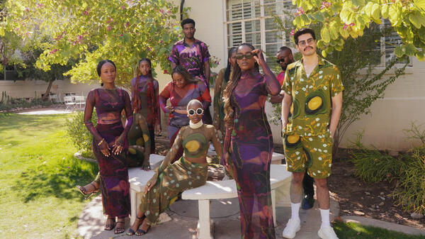 Models in colorful clothing pose in an outdoor setting.