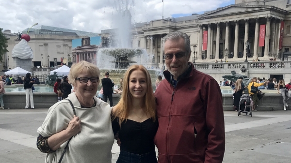 Student posing with grandparents in front of a fountain.