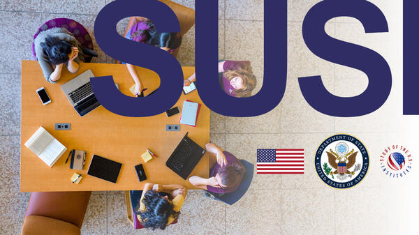 Image of an aerial view of a group of people seated at a table with laptops and papers superimposed with the letters "SUSI."