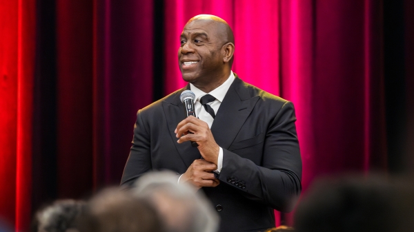 Magic Johnson speaking to audience in front of red curtain backdrop