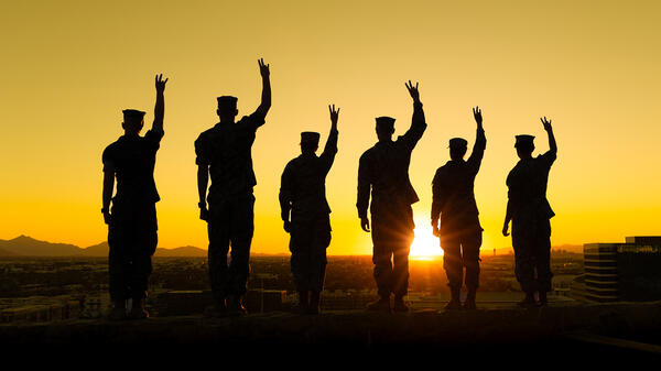 Silhouettes of six people wearing military fatigues while holding up their arms and making the ASU pitchfork symbol with their hands.