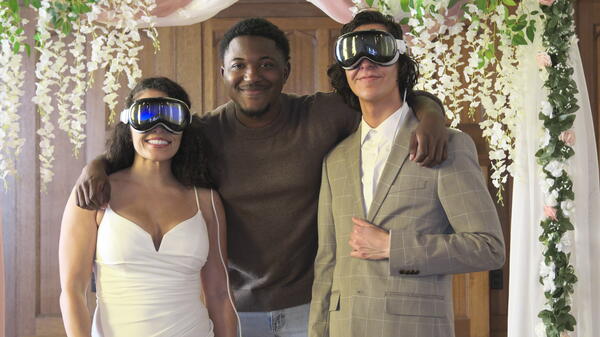 Man and woman wearing wedding attire and large goggles pose with another man.
