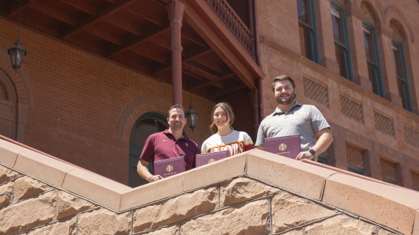 Three people stand on a staircase holding ASU degrees.