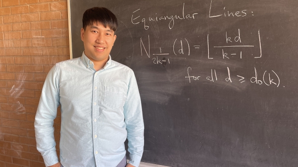 ASU Assistant Professor Zilin Jiang stands next to a chalkboard with math equations on it.