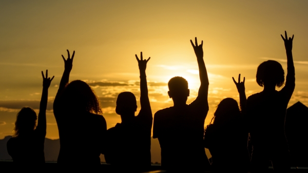 Silhouettes of people holding their arms up and making the ASU pitchfork symbol with their hands.