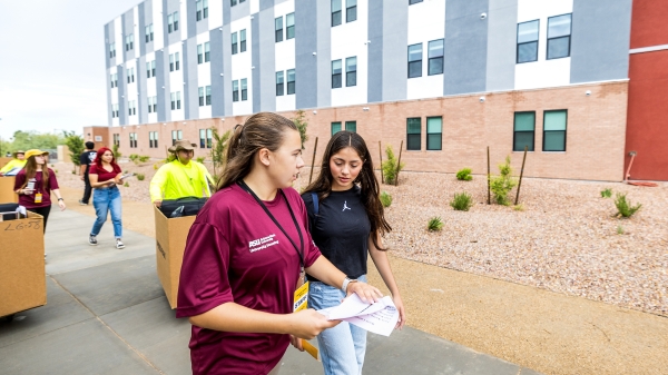 Advisor talks to student as movers follow behind them during move-in day on ASU's West Valley campus