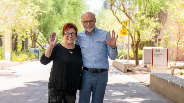 A woman and a man pose for a photo while waving at the camera