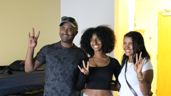 Student and her parents pose for a photo in a dorm room while making a pitchfork with their hands