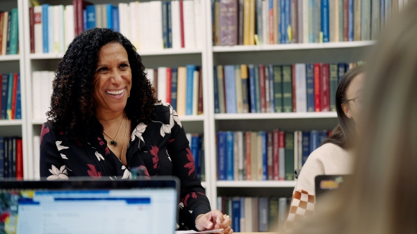 Woman sitting with others at table smiling with bookcases behind her