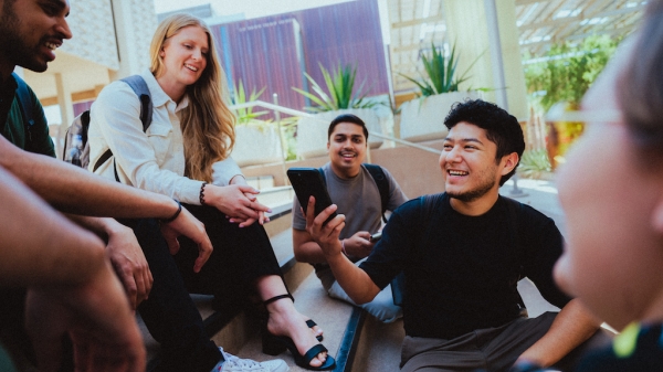 Students sitting on stairs, one holding a cell phone.