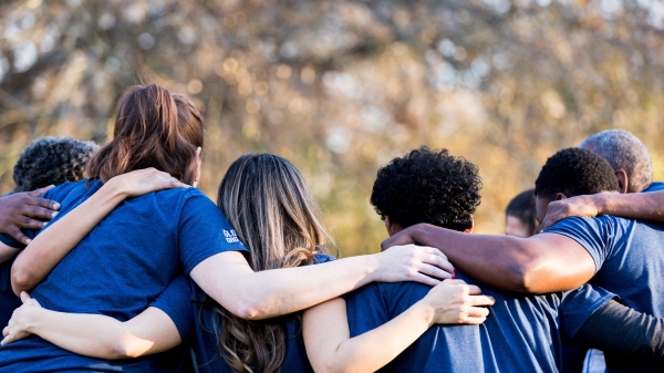 Backs of people wearing blue shirts with arms around each other.