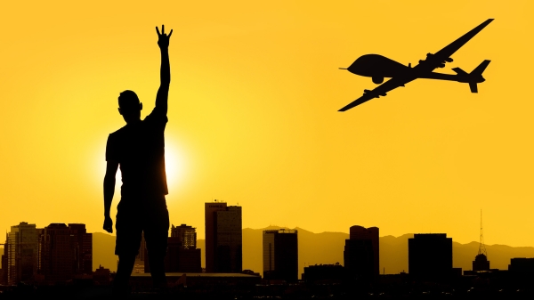 An ASU student gives the forks up gesture in silhouette at sunset as a drone cruises across the Phoenix, Arizona skyline.