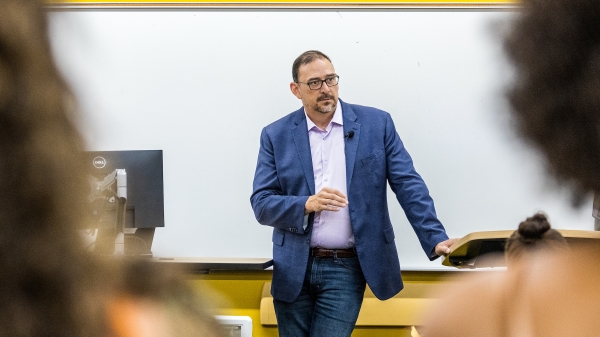 Man in blue suit standing in front of college students in classroom