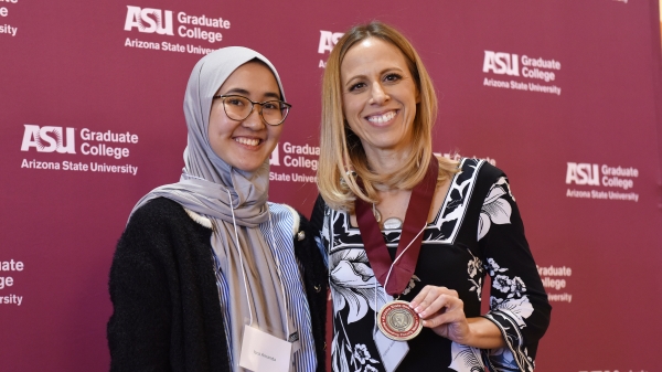 Two women smile at the camera as one holds a medal.