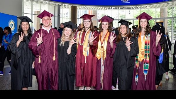 Group of ASU graduates wearing graduation gowns and hats pose doing the forks-up hand sign.