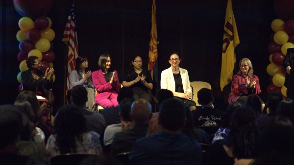 People sitting onstage in front of a crowd with ASU balloons and flags around them.