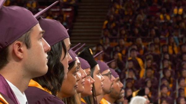 Graduates in caps and gowns look to an off-camera stage