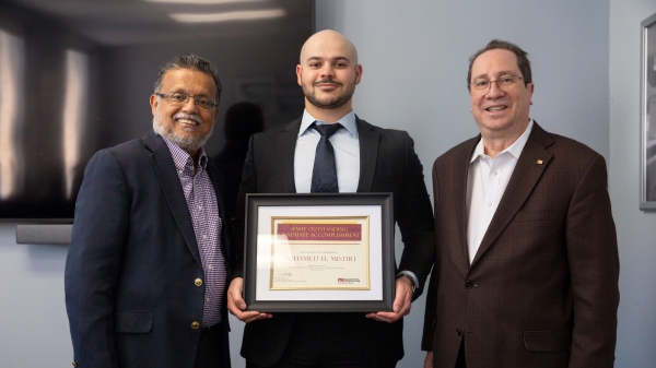 Three men posing for a photo as the man in the middle holds an award.