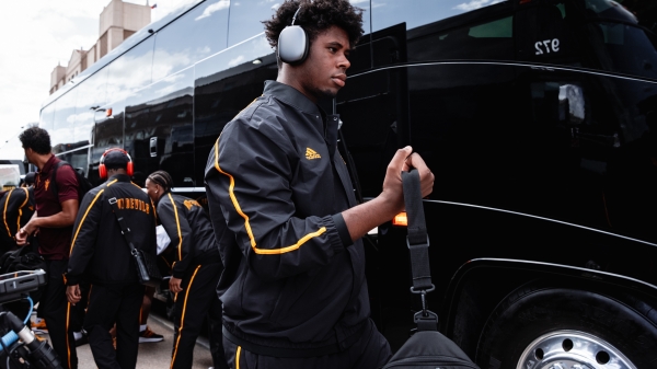 ASU football players in track suits board black charter buses