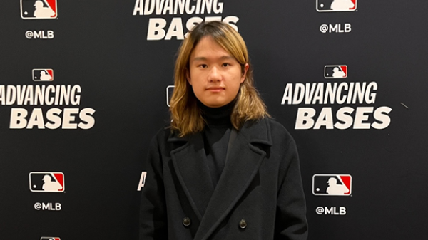 Sungkwon in a black coat stands before a backdrop with Major League Baseball (MLB) logos. 