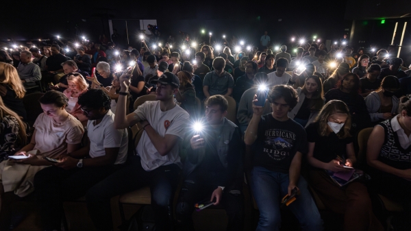 A crowd in a darkened room hold up their phone flashlights