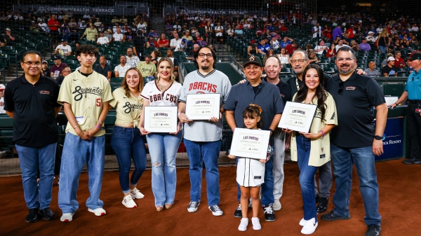 Group of people pose for a photo, some holding awards, in front of a stadium audience